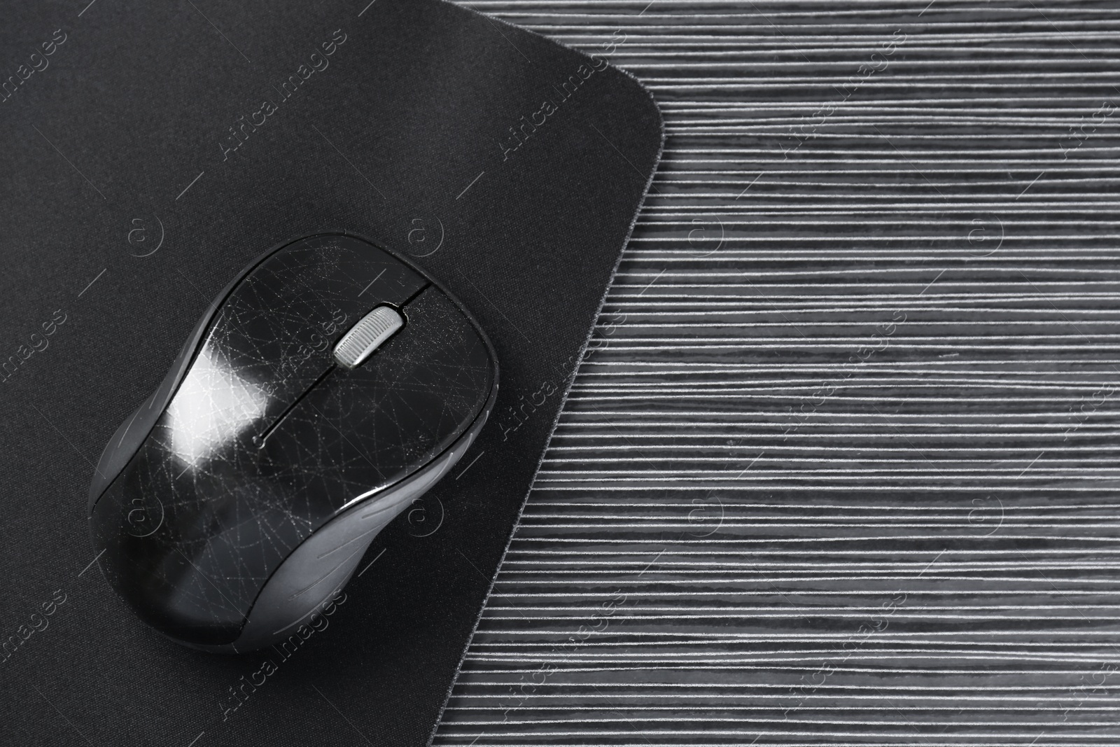 Photo of Computer mouse with mousepad on black wooden table, top view. Space for text