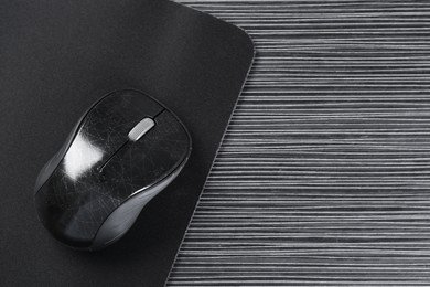 Photo of Computer mouse with mousepad on black wooden table, top view. Space for text