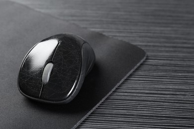 Photo of Computer mouse with mousepad on black wooden table, closeup. Space for text