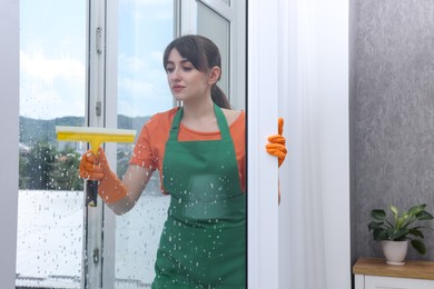 Young housewife with squeegee cleaning window indoors