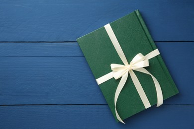 Photo of Book tied with beige ribbon as gift on blue wooden table, top view. Space for text