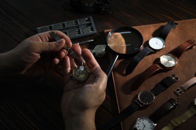 Photo of Man fixing mechanism of vintage wrist watch at wooden table, closeup