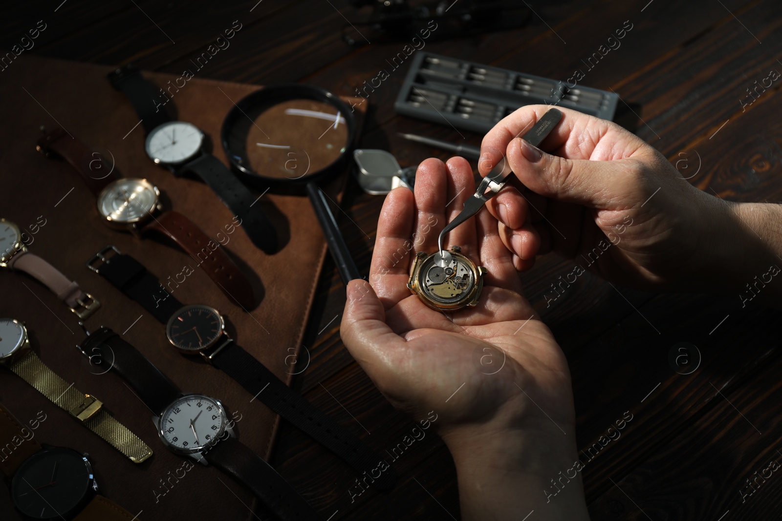 Photo of Man fixing mechanism of vintage wrist watch at wooden table, closeup