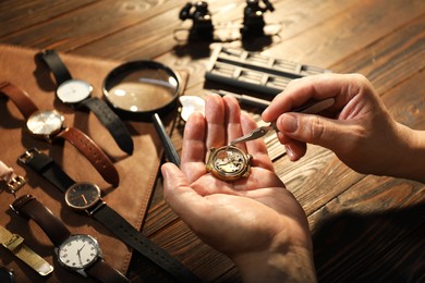 Photo of Man fixing mechanism of vintage wrist watch at wooden table, closeup