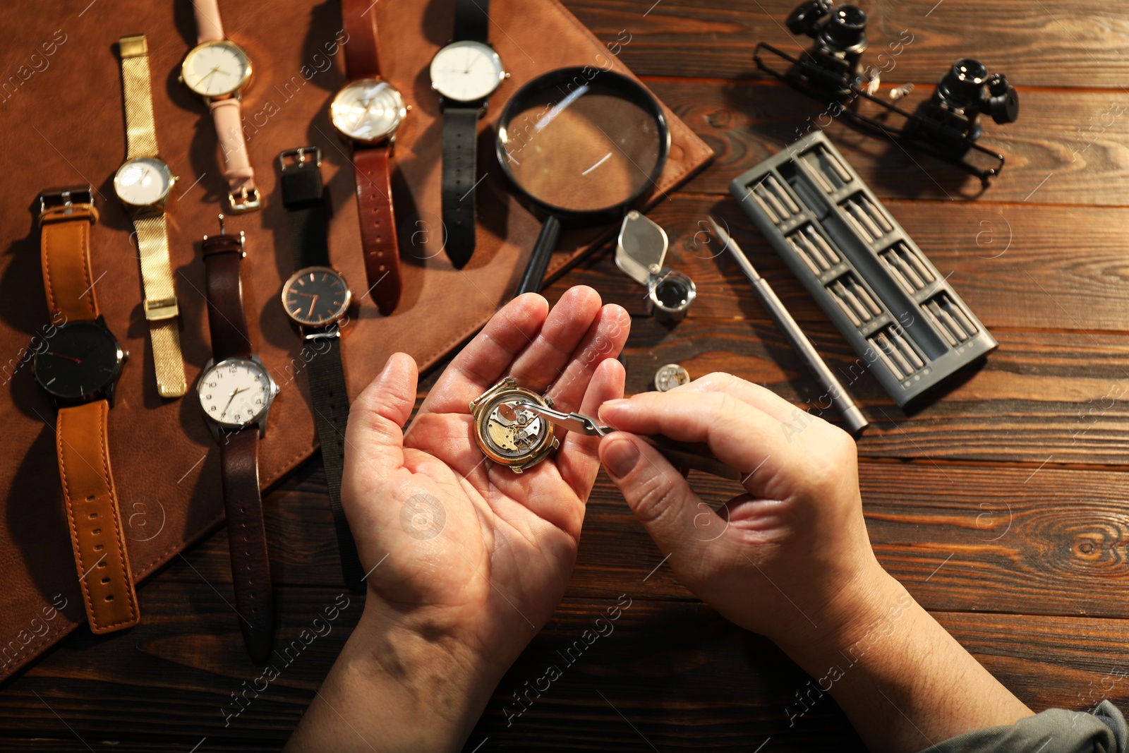 Photo of Man fixing mechanism of vintage wrist watch at wooden table, top view