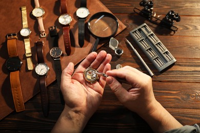 Photo of Man fixing mechanism of vintage wrist watch at wooden table, top view