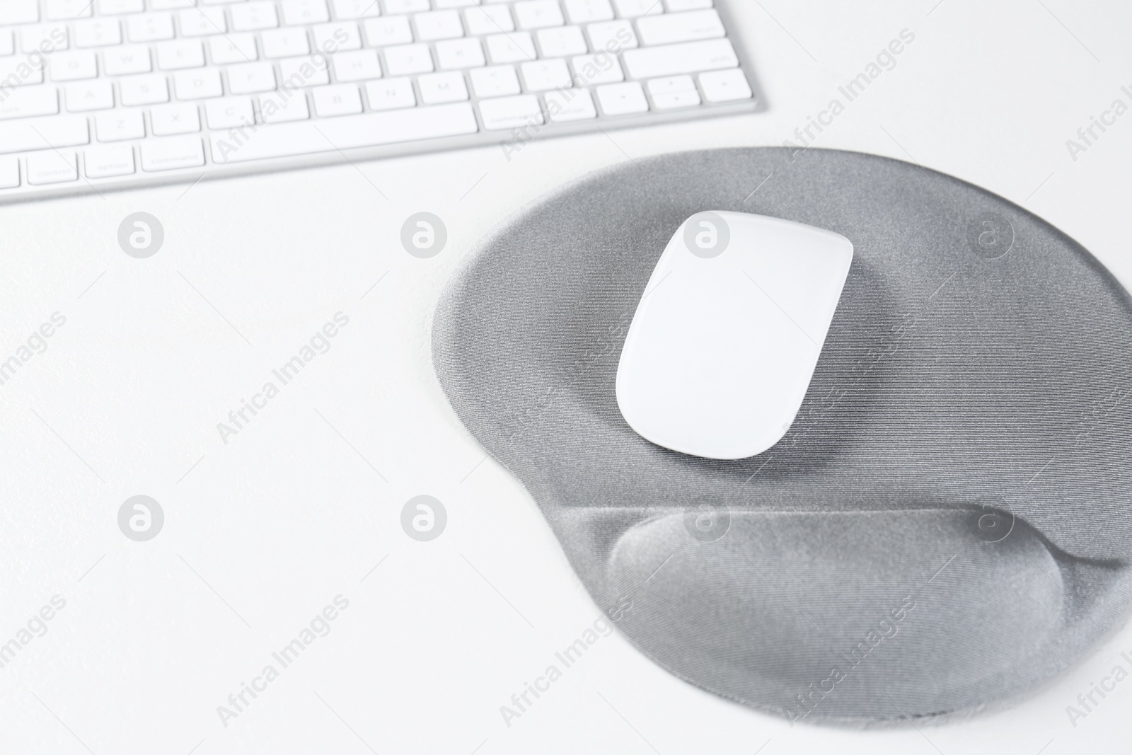 Photo of Keyboard, mouse and mousepad with arm rest on white table, closeup. Space for text