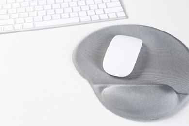 Photo of Keyboard, mouse and mousepad with arm rest on white table, closeup. Space for text