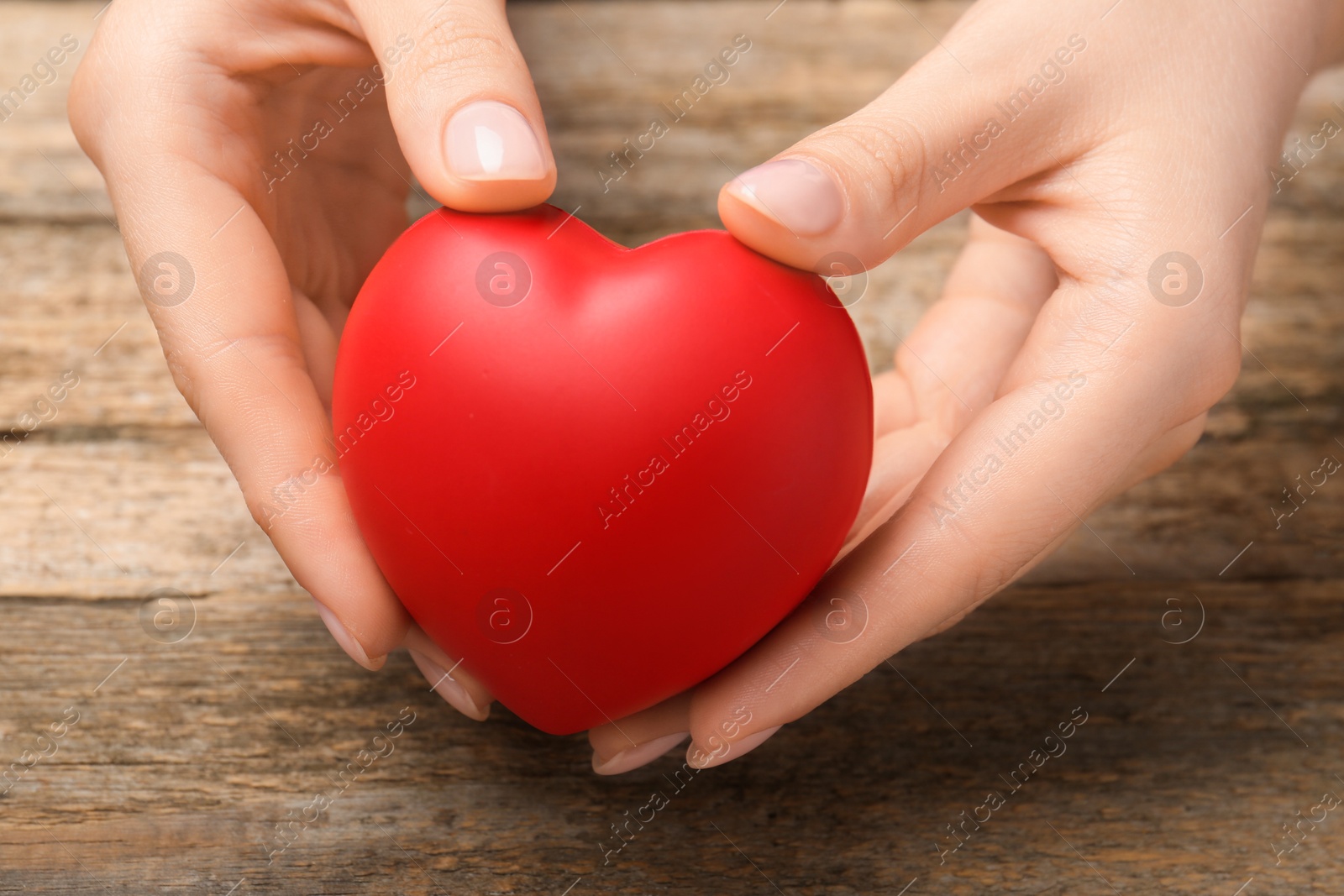 Photo of Woman with red decorative heart at wooden table, closeup