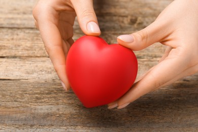 Photo of Woman with red decorative heart at wooden table, closeup