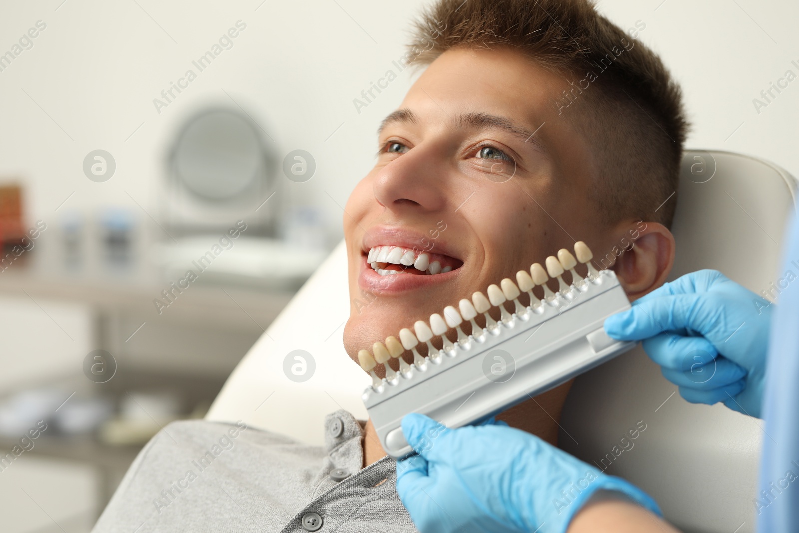 Photo of Doctor checking young man's teeth color in clinic, closeup. Dental veneers