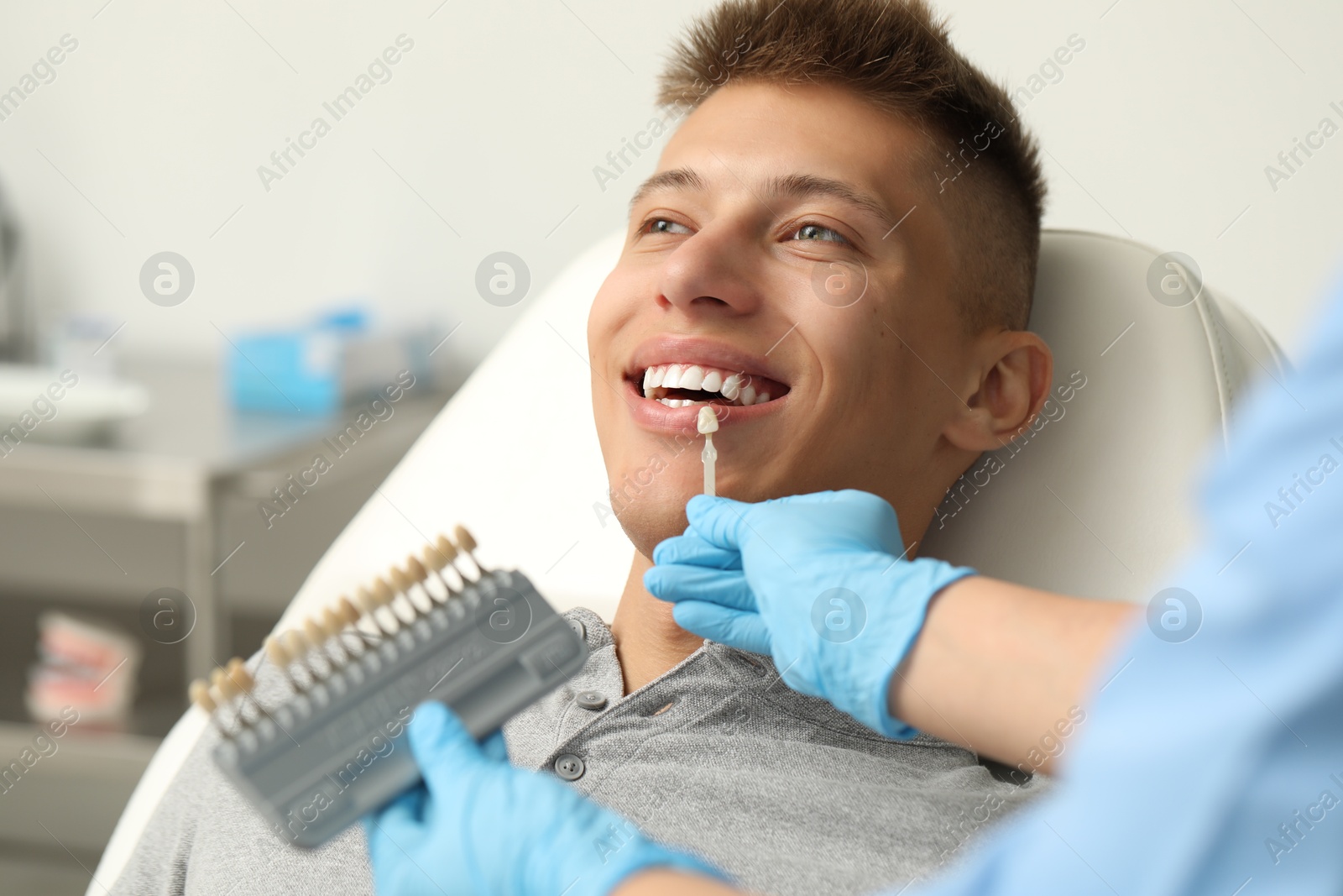 Photo of Doctor checking young man's teeth color in clinic, closeup. Dental veneers