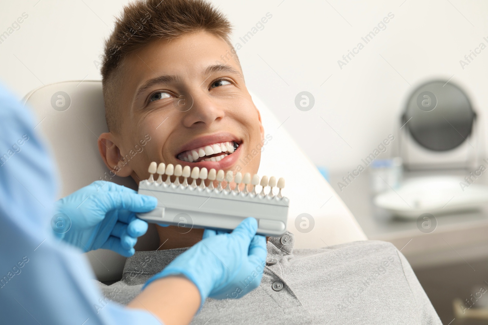 Photo of Doctor checking young man's teeth color in clinic, closeup. Dental veneers