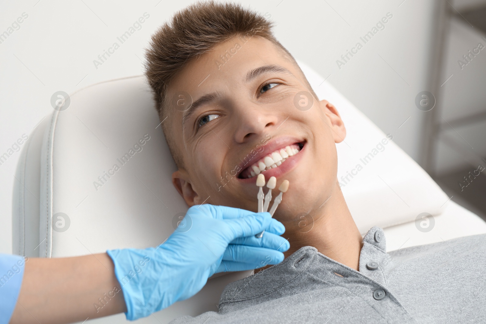 Photo of Doctor checking young man's teeth color in clinic, closeup. Dental veneers