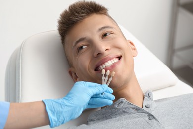 Photo of Doctor checking young man's teeth color in clinic, closeup. Dental veneers