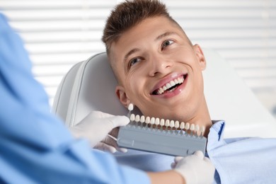 Doctor checking young man's teeth color in clinic, closeup. Dental veneers