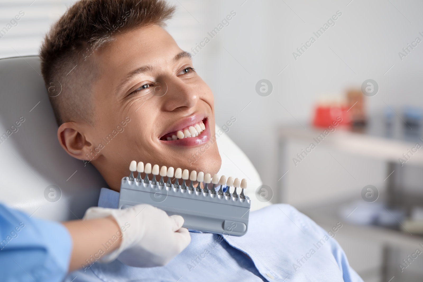 Photo of Doctor checking young man's teeth color in clinic, closeup. Dental veneers