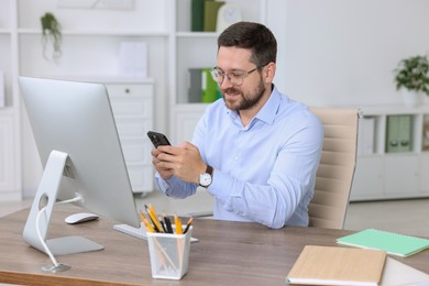 Smiling businessman using smartphone at table in office