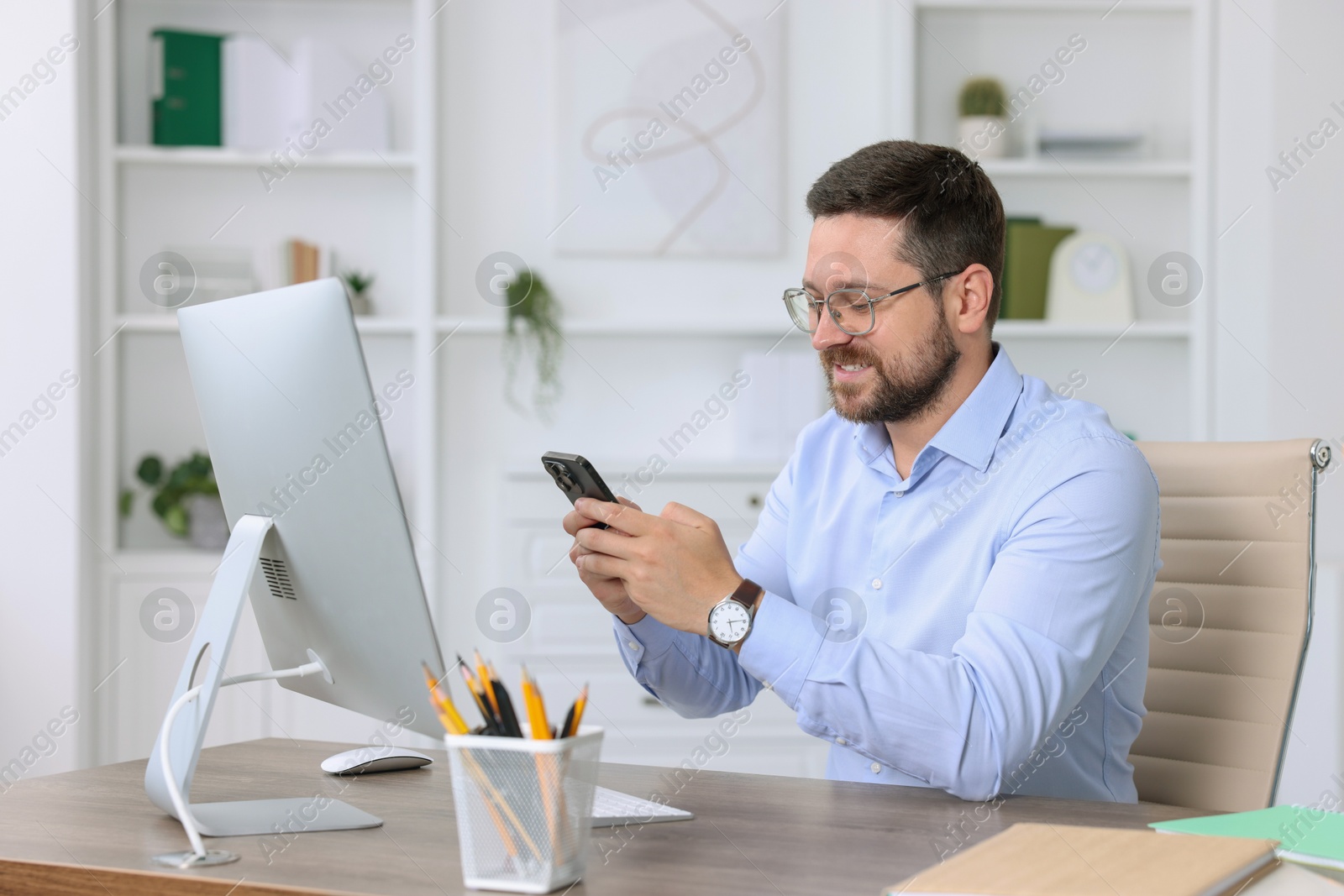 Photo of Smiling businessman using smartphone at table in office