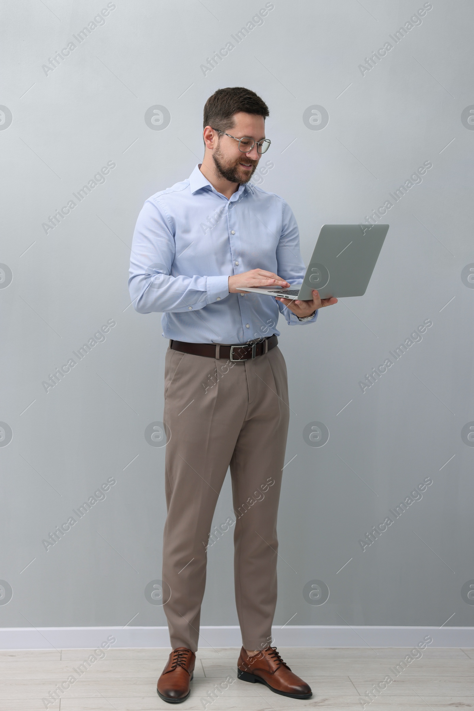 Photo of Businessman using laptop near grey wall indoors