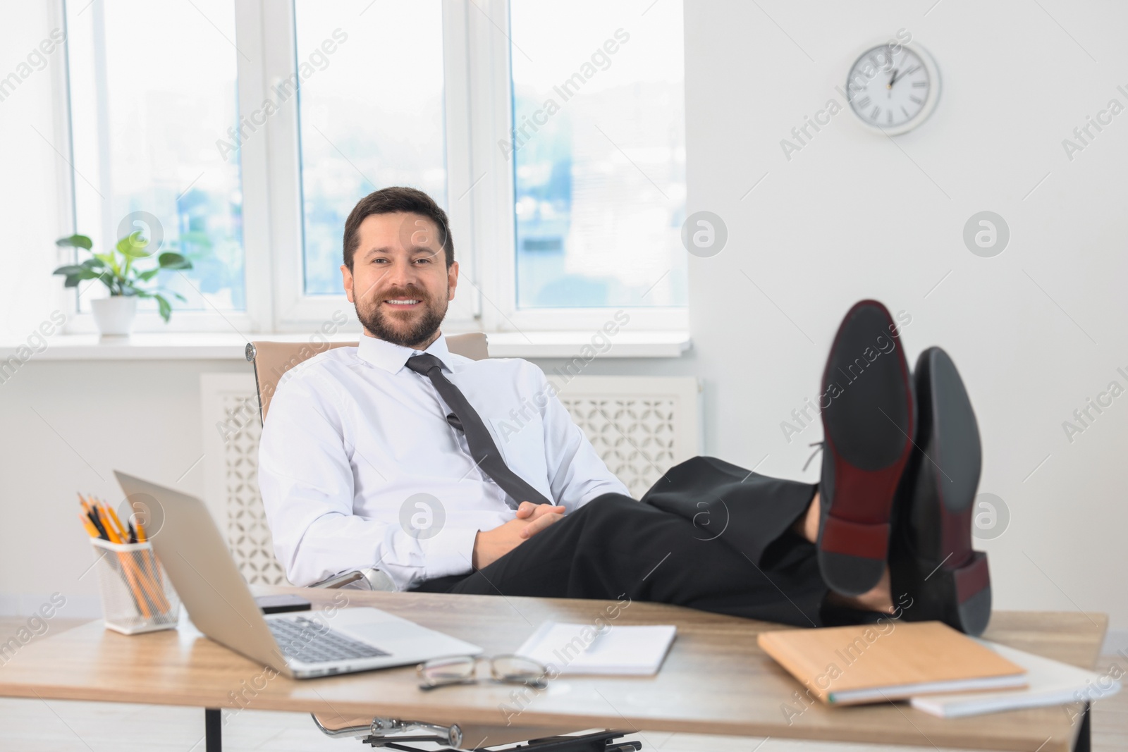 Photo of Smiling businessman holding legs on table in office. Break time