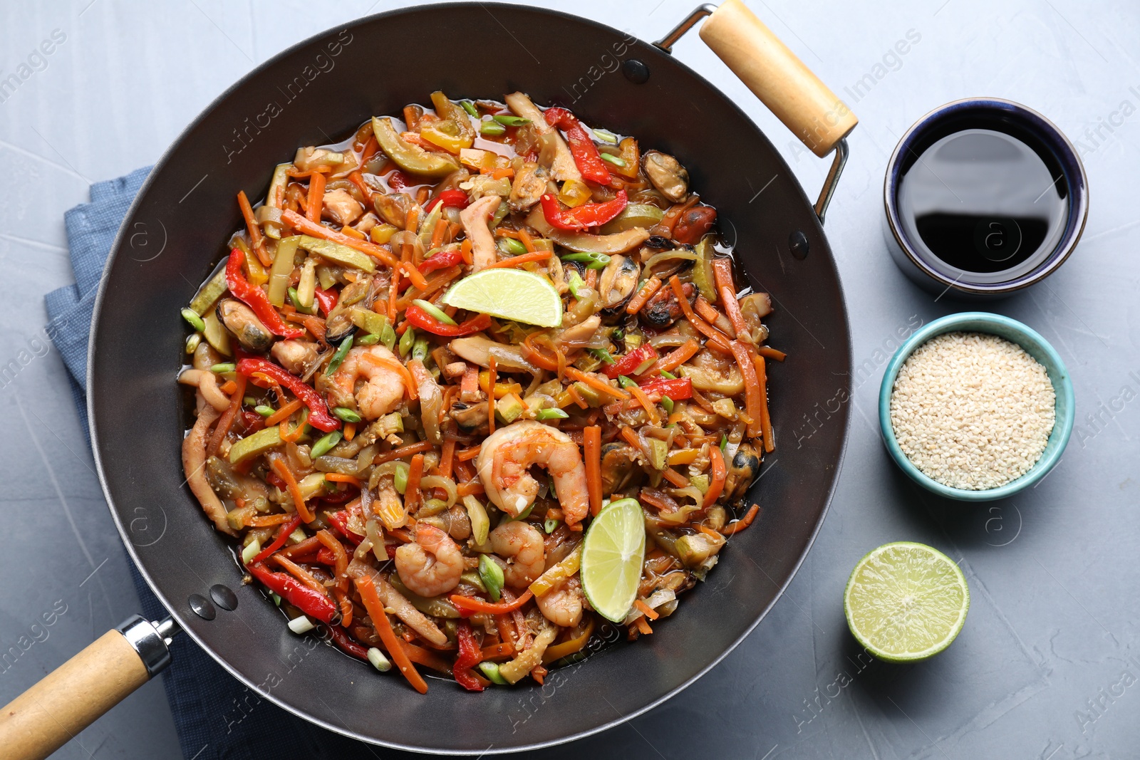 Photo of Stir-fry sea food in wok served on grey table, flat lay