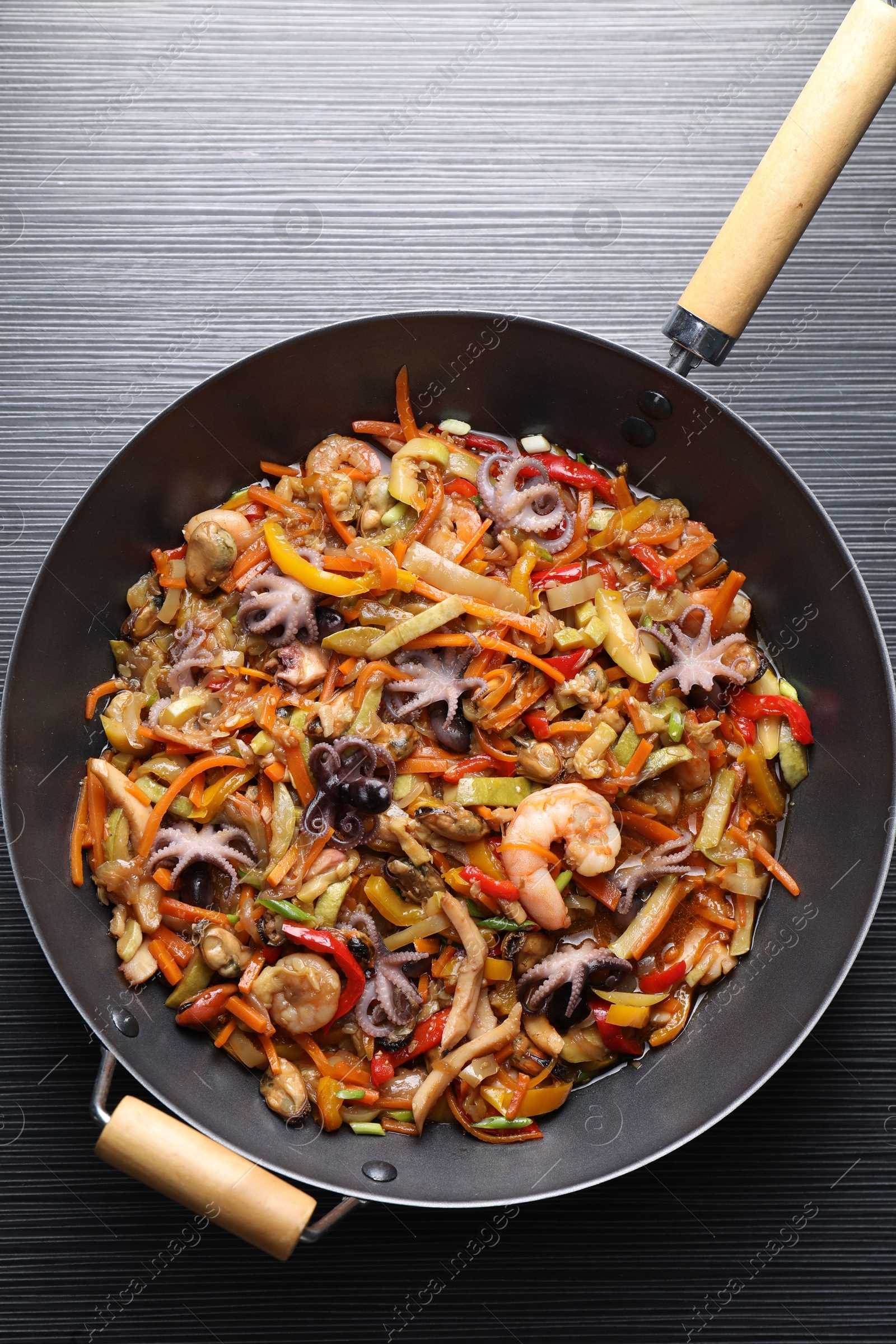 Photo of Stir-fry sea food in wok on black wooden table, top view