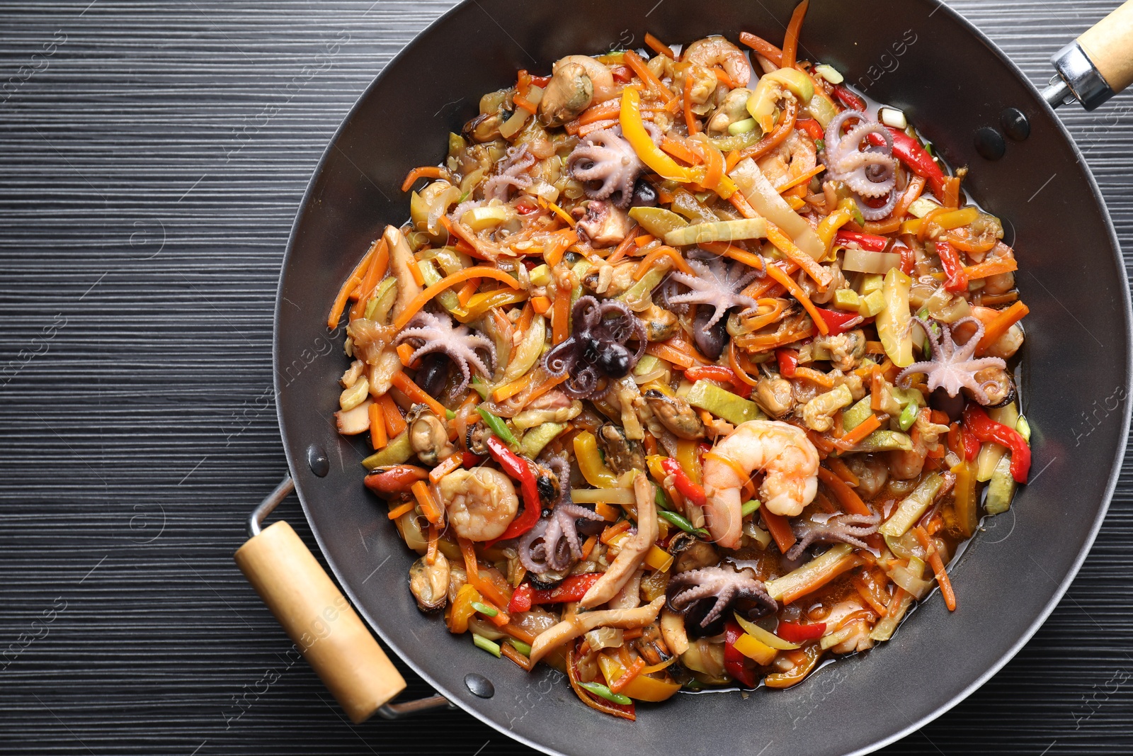 Photo of Stir-fry sea food in wok on black wooden table, top view