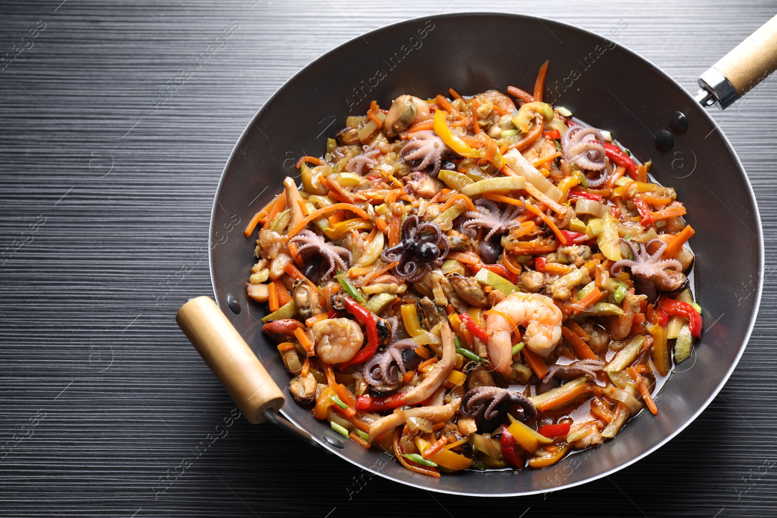 Photo of Stir-fry sea food in wok on black wooden table