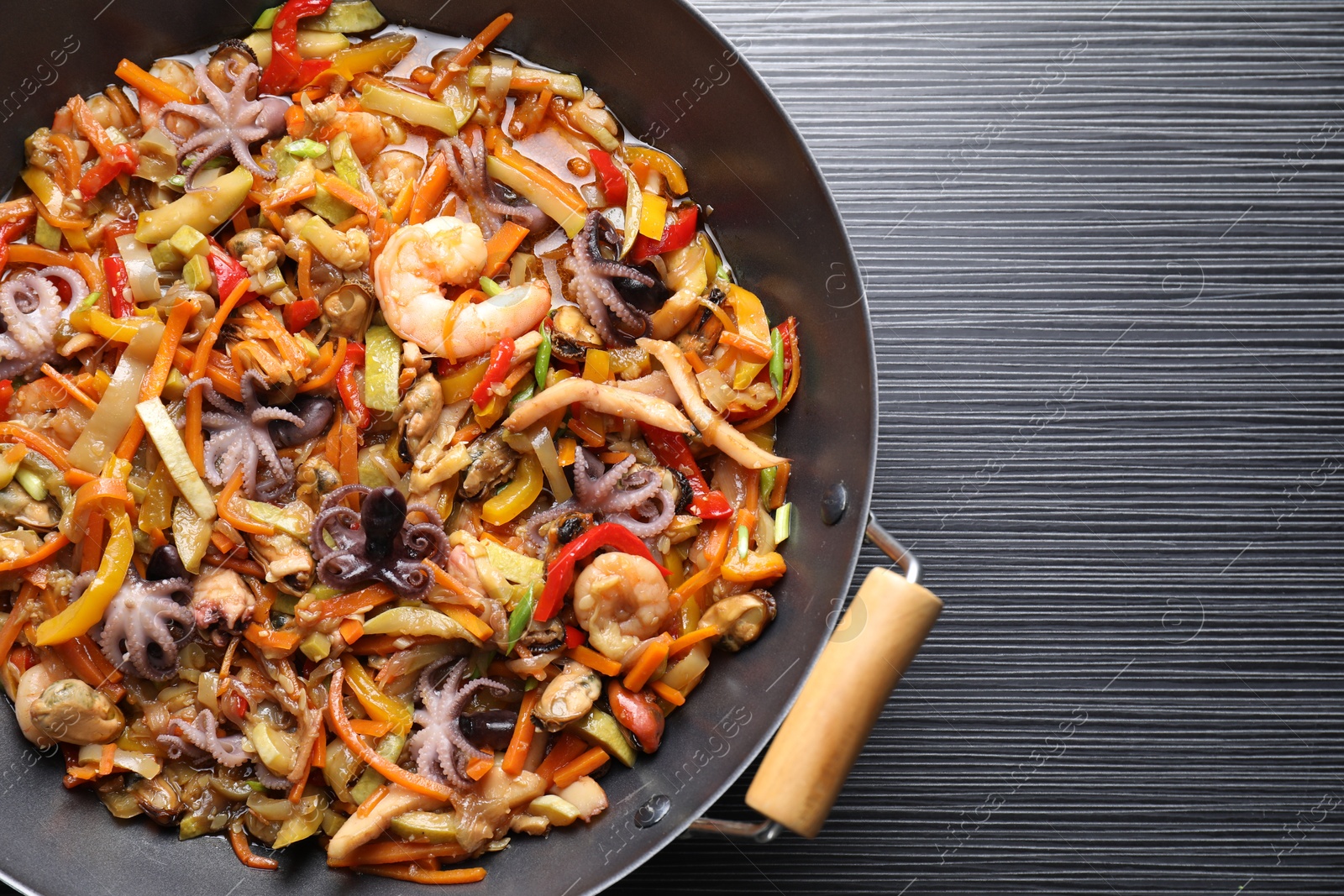 Photo of Stir-fry sea food in wok on black wooden table, top view. Space for text