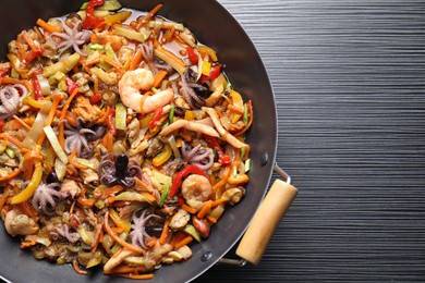 Photo of Stir-fry sea food in wok on black wooden table, top view. Space for text