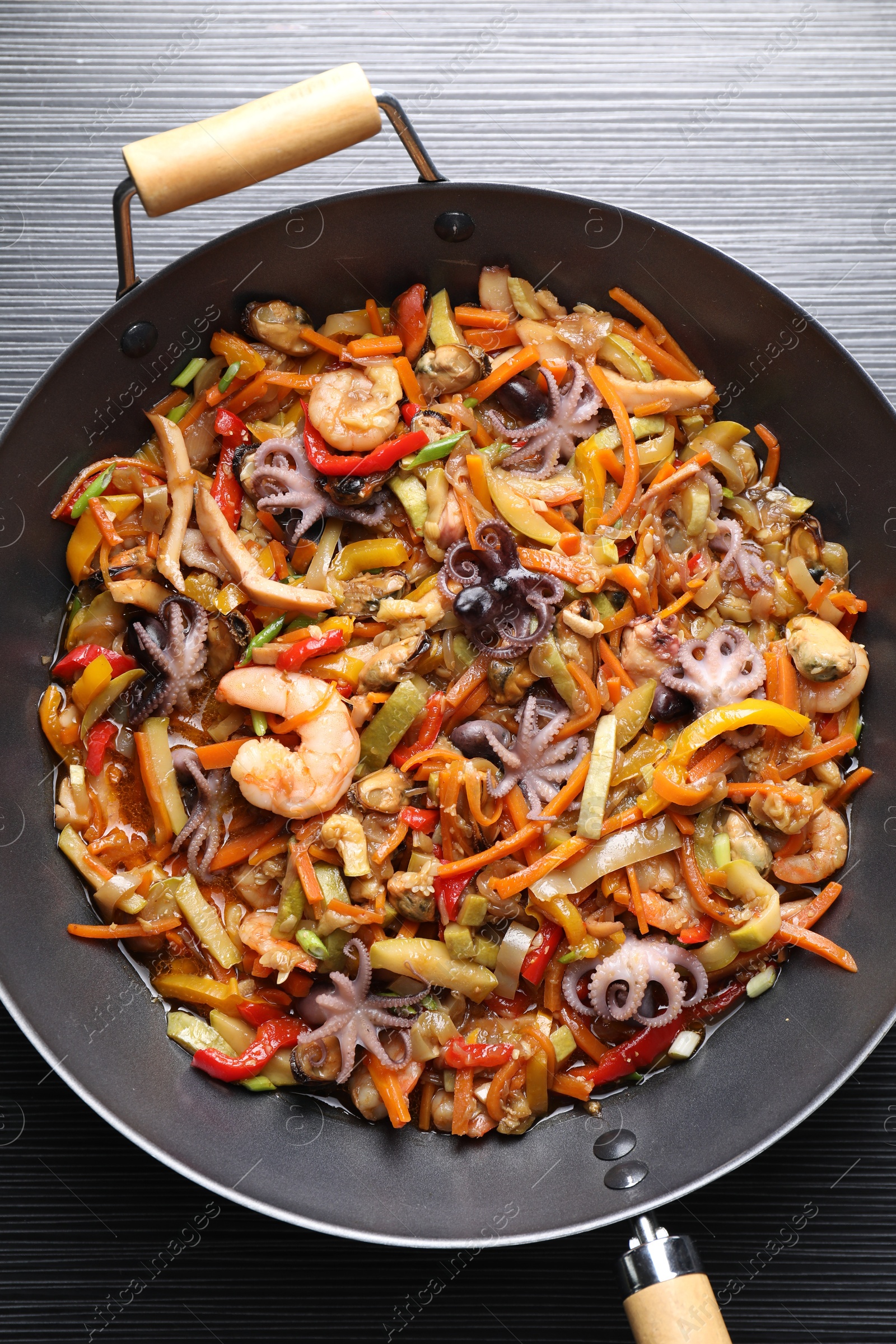 Photo of Stir-fry sea food in wok on black wooden table, top view