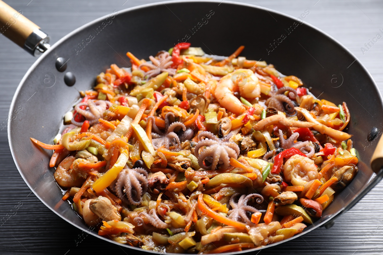 Photo of Stir-fry sea food in wok on black wooden table, closeup