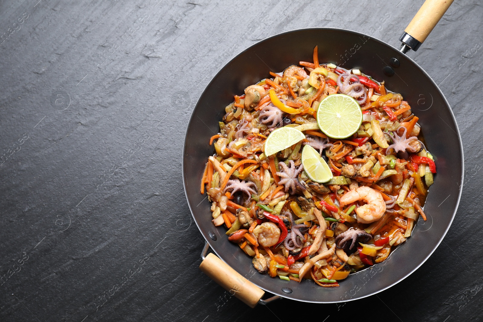 Photo of Stir-fry sea food in wok on grey textured table, top view. Space for text