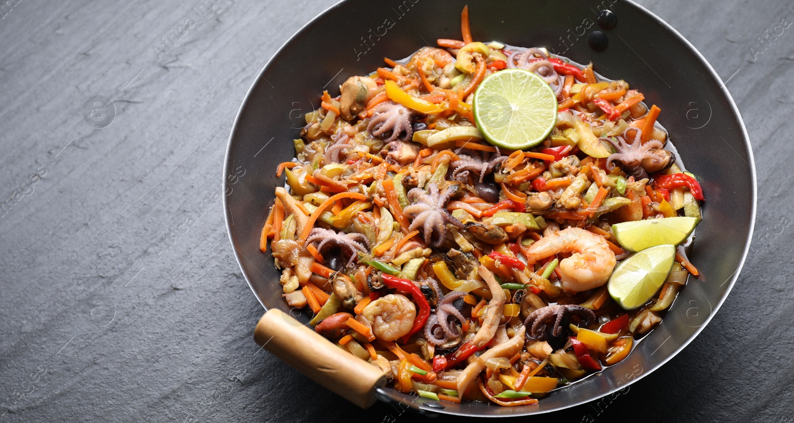 Photo of Stir-fry sea food in wok on grey textured table