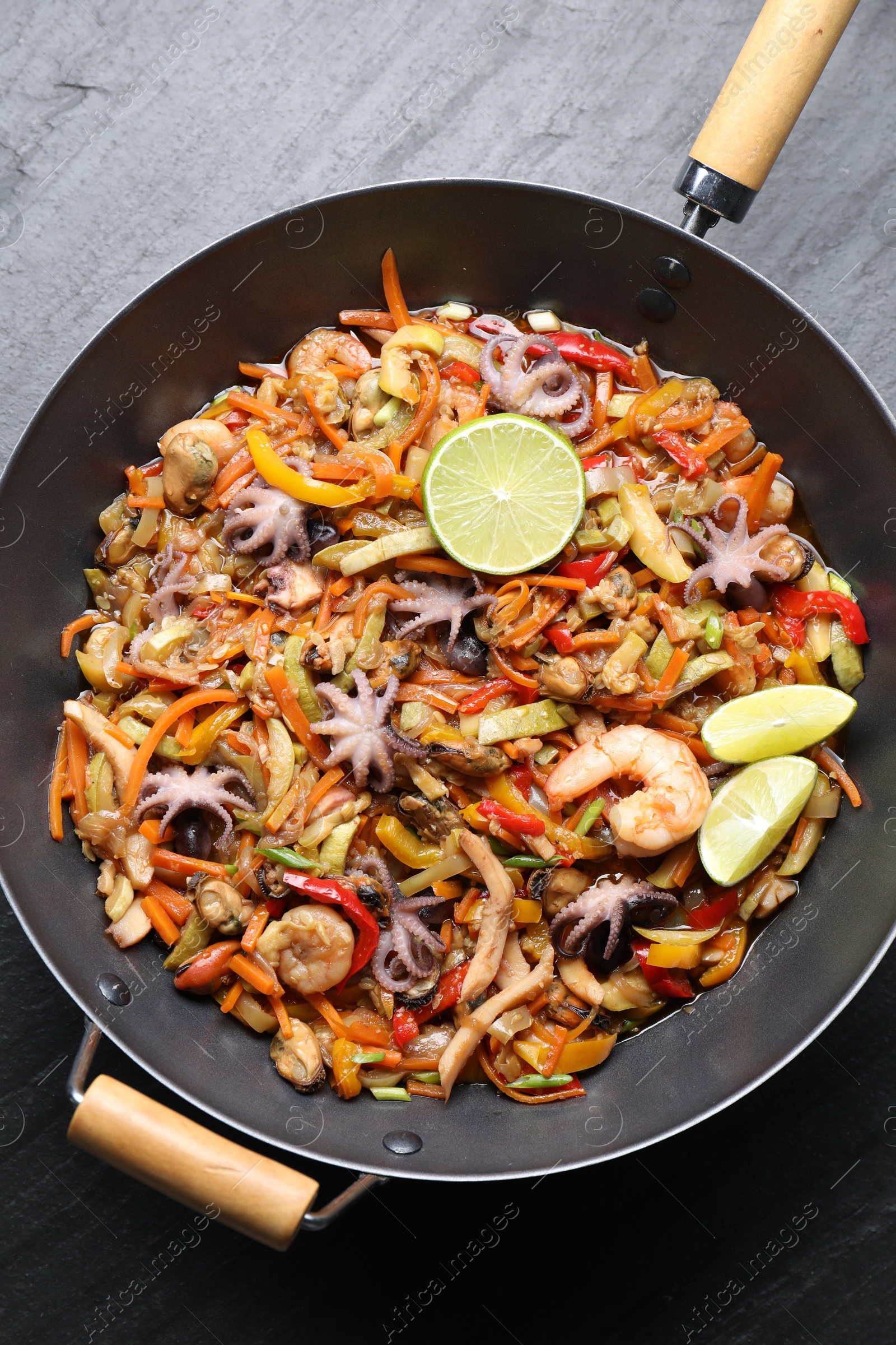 Photo of Stir-fry sea food in wok on grey textured table, top view