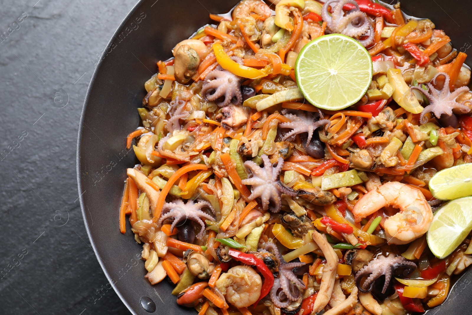 Photo of Stir-fry sea food in wok on grey textured table, top view