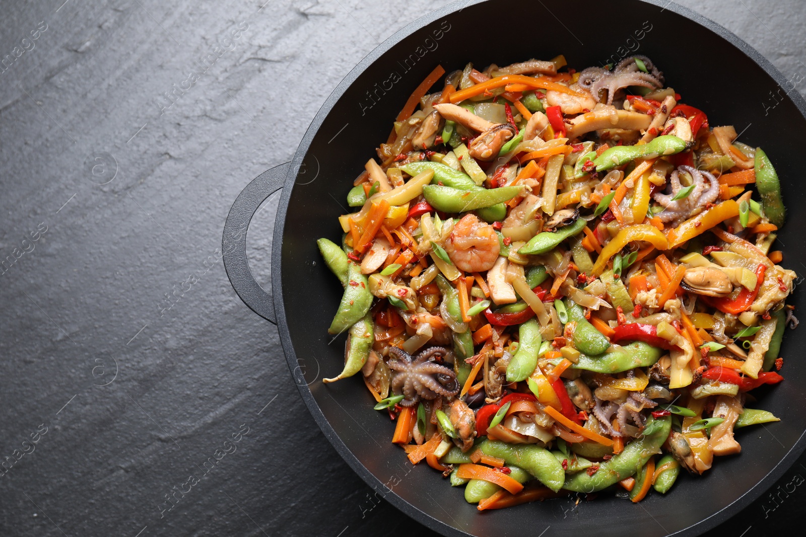 Photo of Stir-fry sea food in wok on grey textured table, top view. Space for text