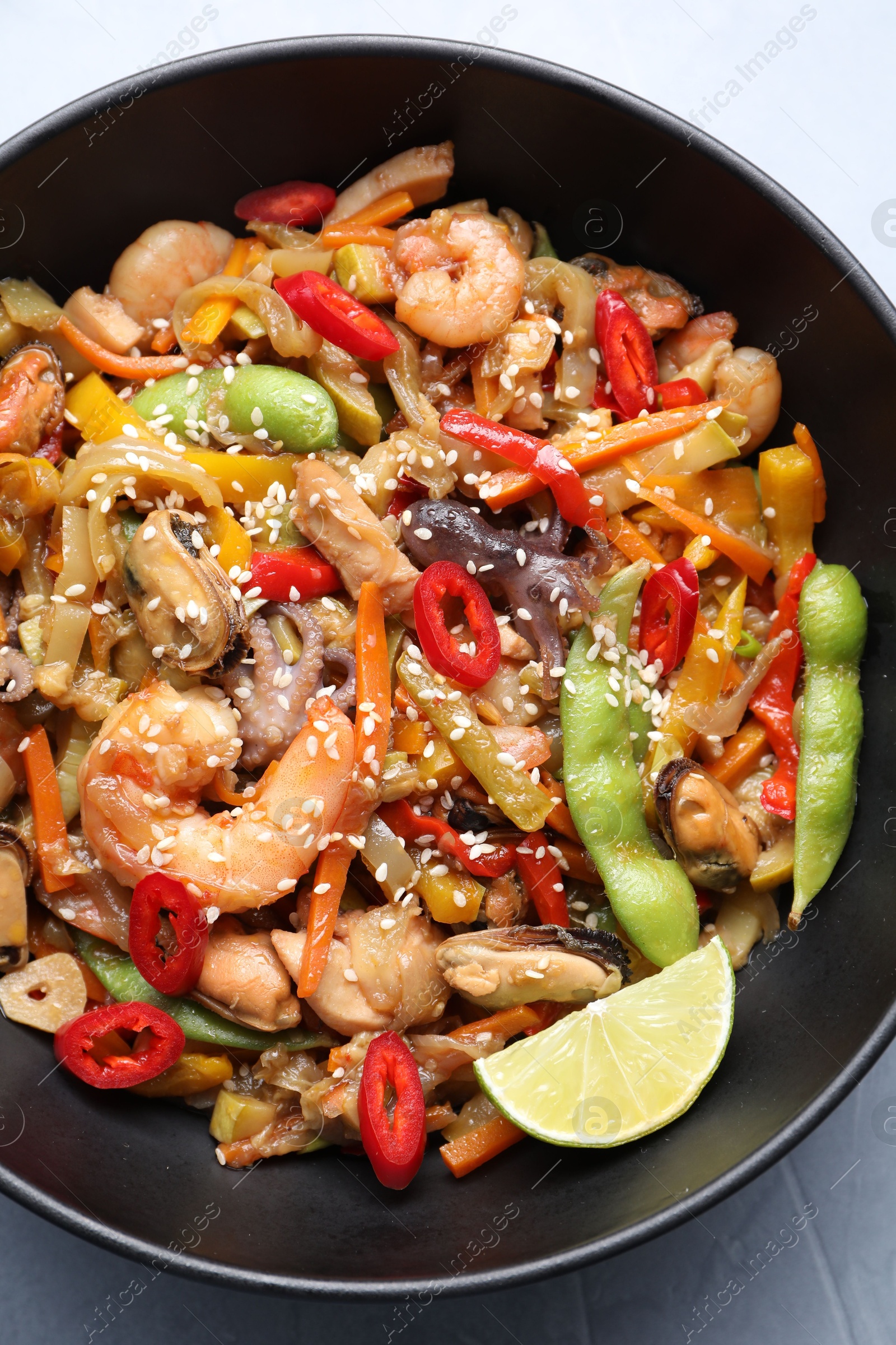 Photo of Stir-fry sea food in bowl on light grey table, top view