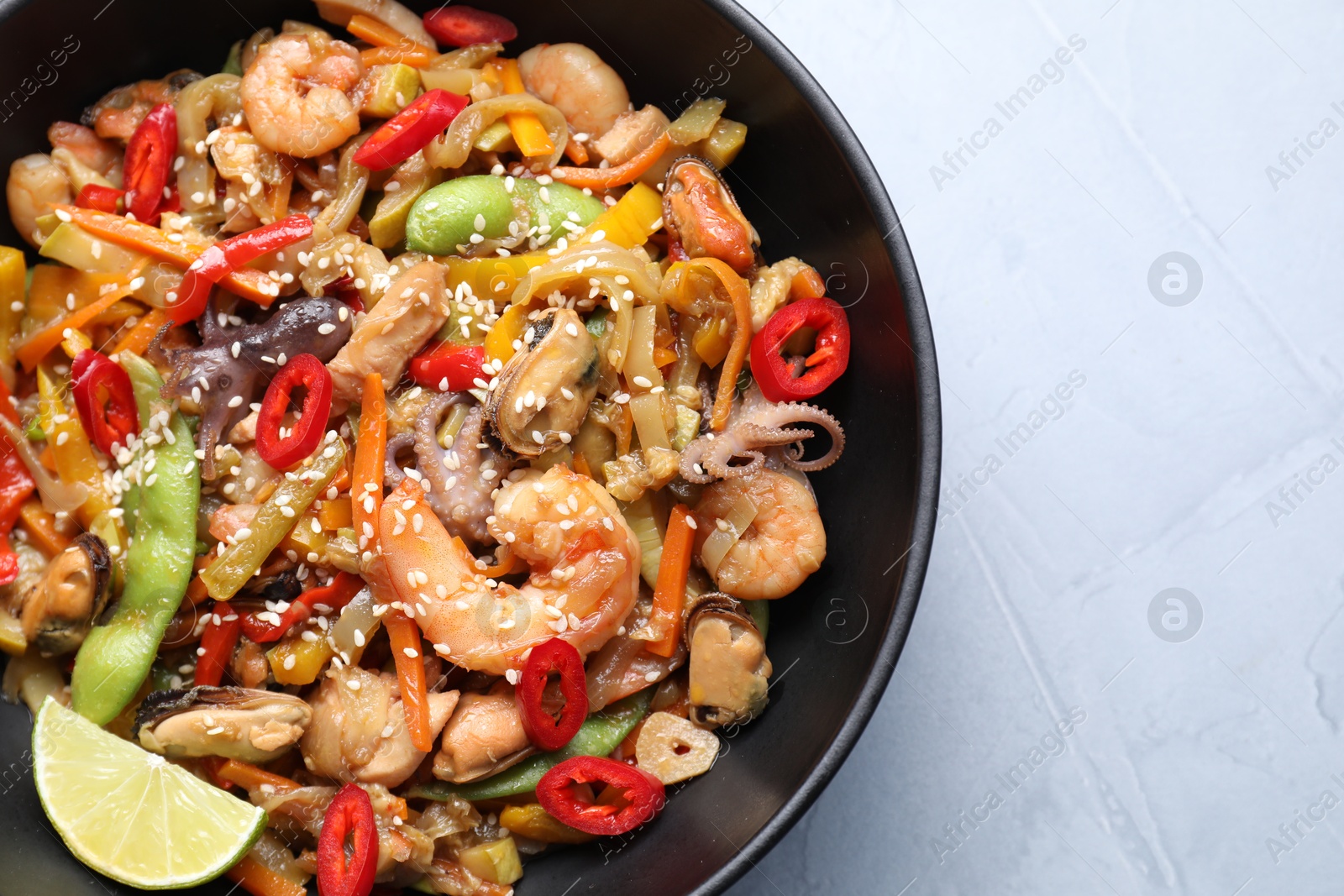 Photo of Stir-fry sea food in bowl on light grey table, top view. Space for text