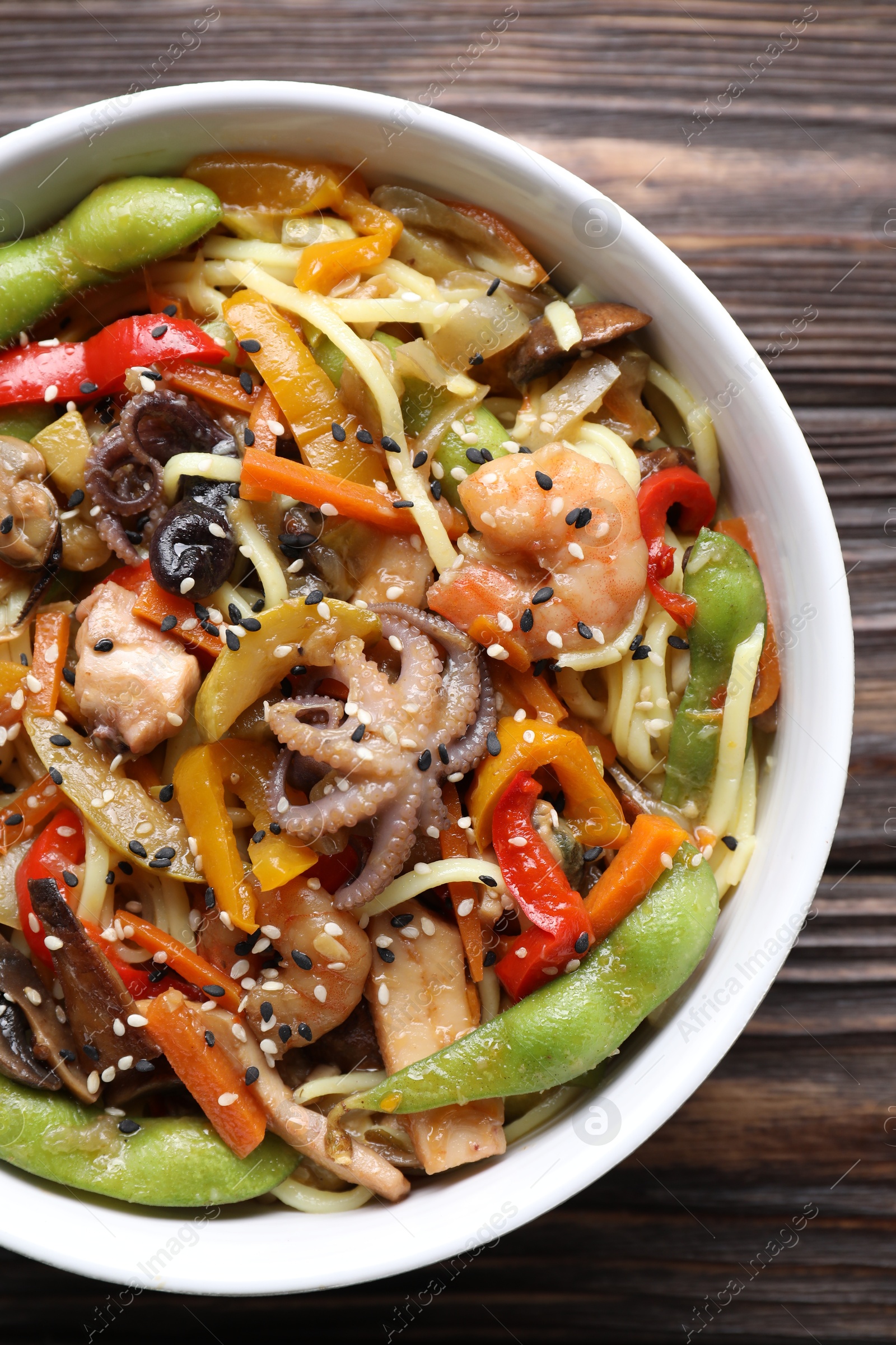 Photo of Stir-fry noodles with sea food in bowl on wooden table, top view