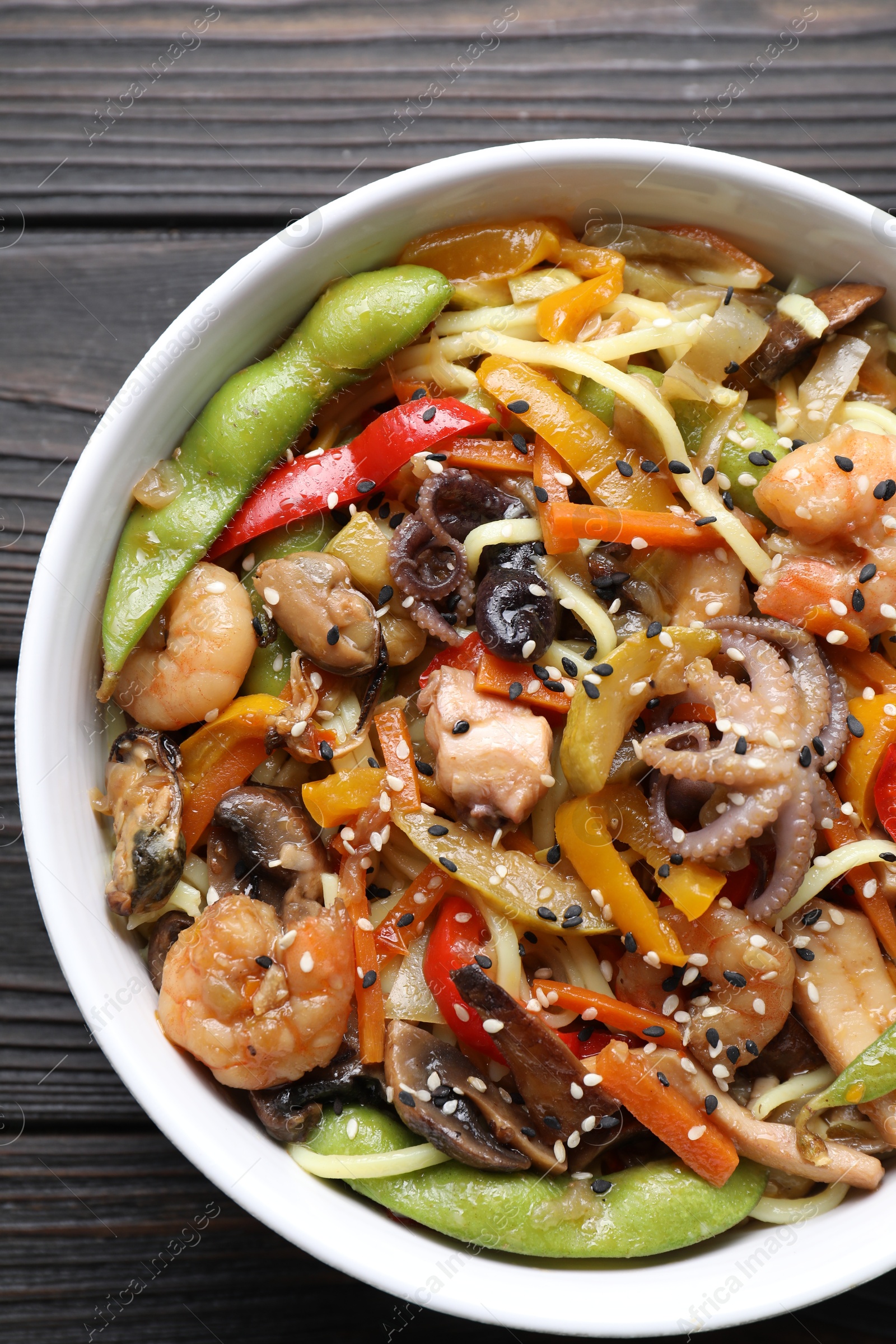 Photo of Stir-fry noodles with sea food in bowl on wooden table, top view