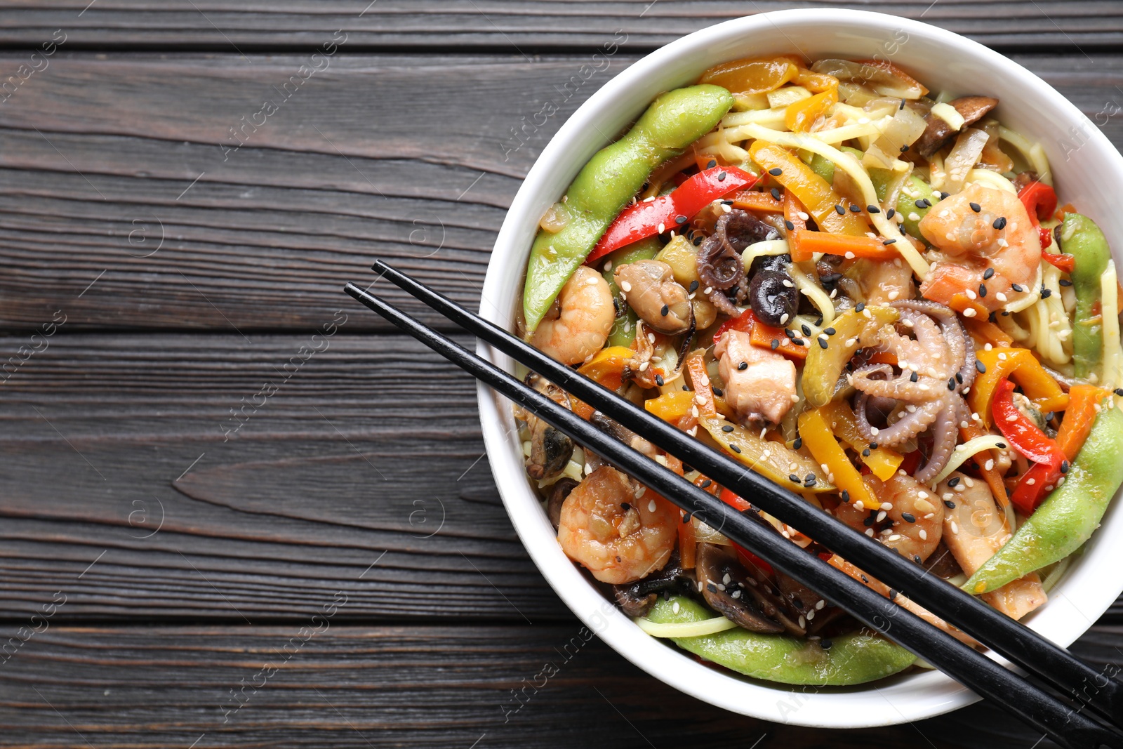 Photo of Stir-fry noodles with sea food in bowl and chopsticks on wooden table, top view. Space for text