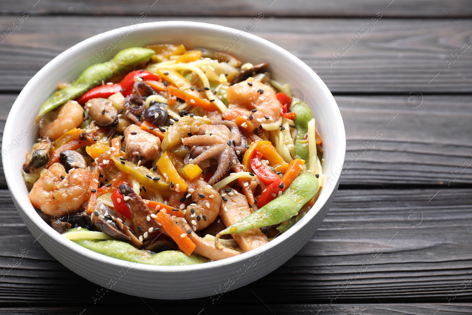 Photo of Stir-fry noodles with sea food in bowl on wooden table, closeup