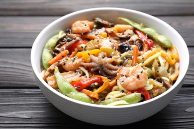 Photo of Stir-fry noodles with sea food in bowl on wooden table, closeup