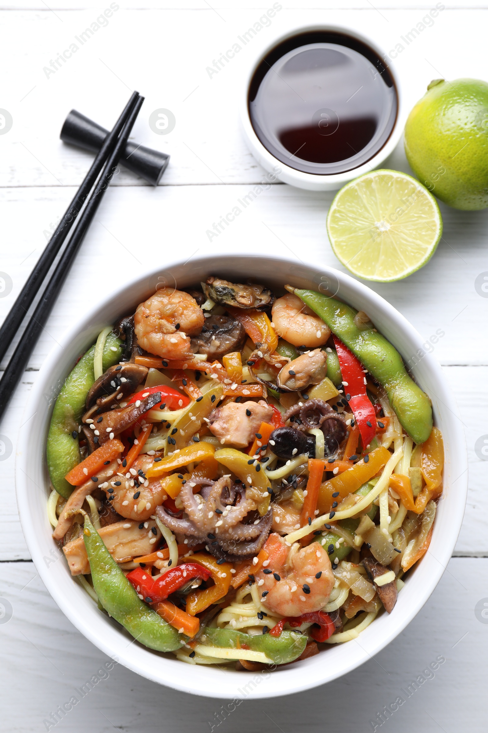 Photo of Stir-fry noodles with sea food served on white wooden table, flat lay