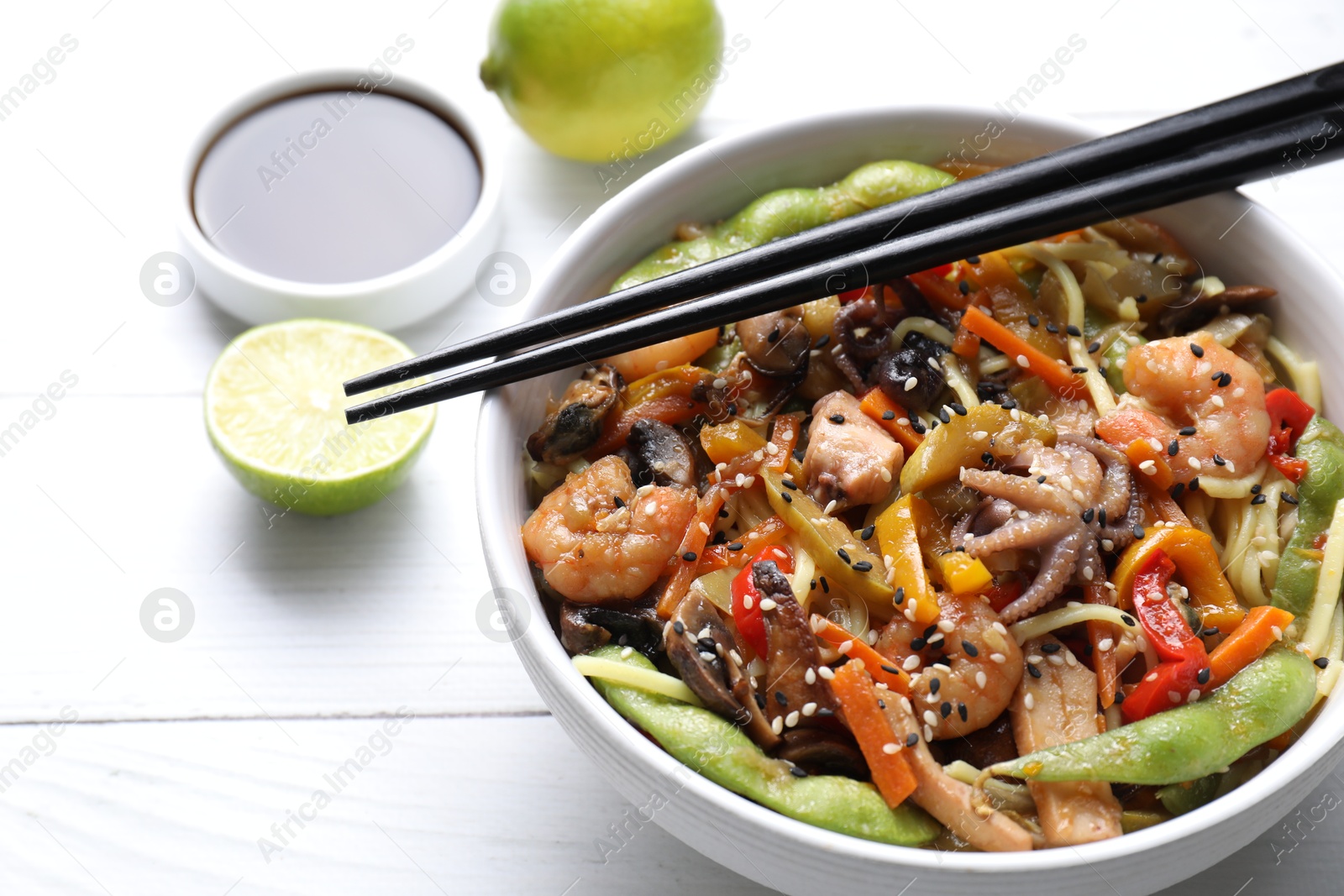 Photo of Stir-fry noodles with sea food served on white wooden table, closeup