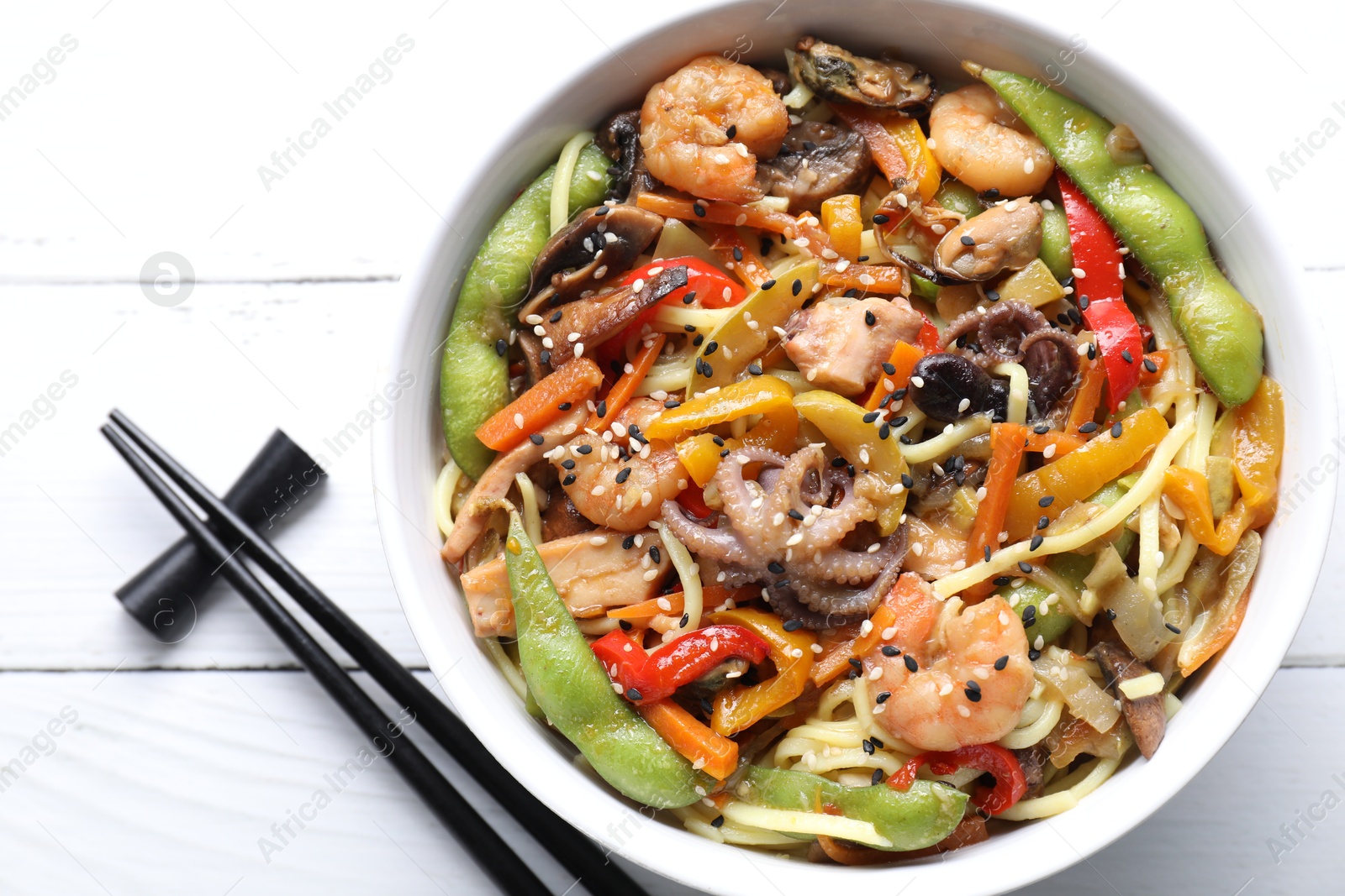 Photo of Stir-fry noodles with sea food served on white wooden table, flat lay