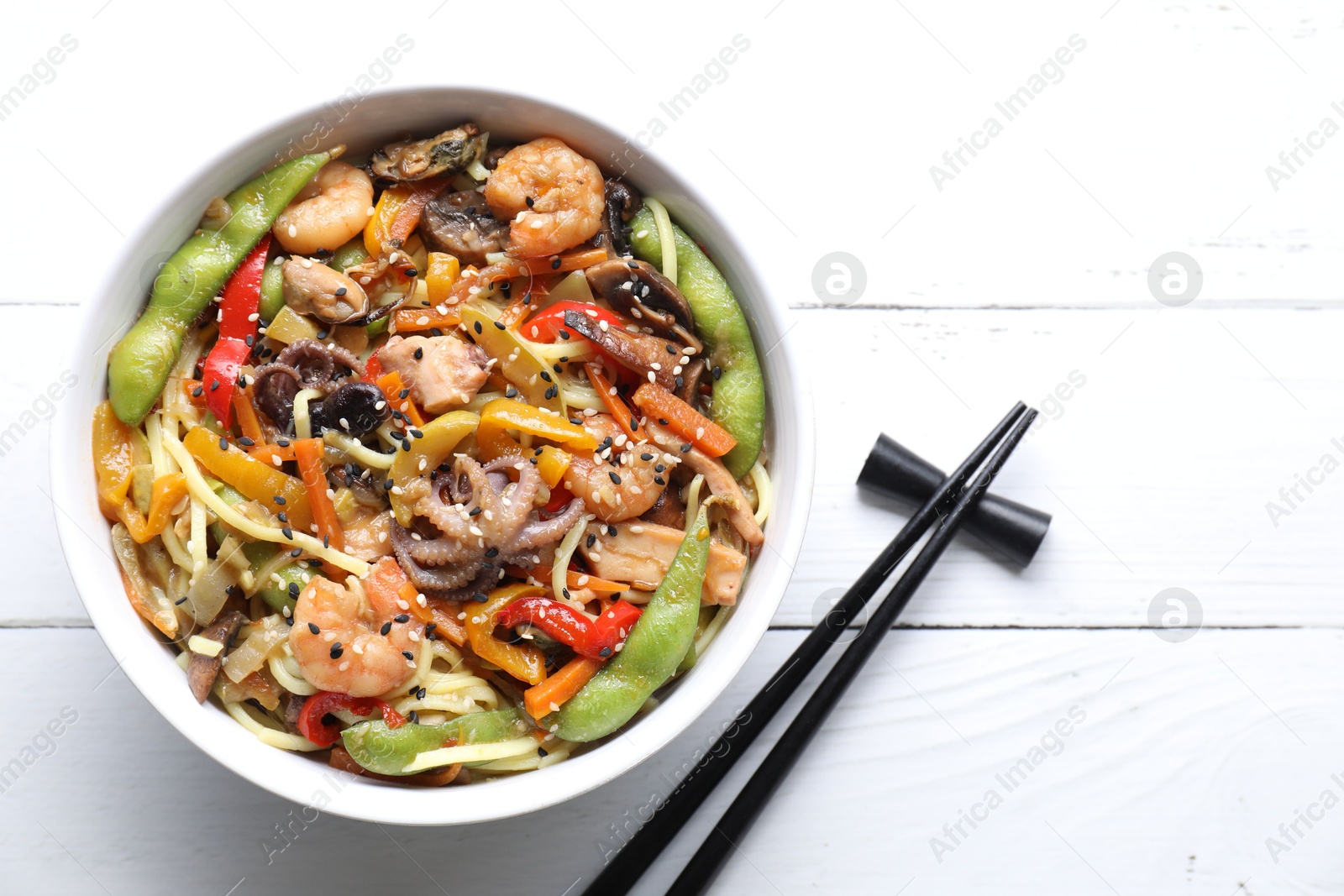 Photo of Stir-fry noodles with sea food served on white wooden table, flat lay