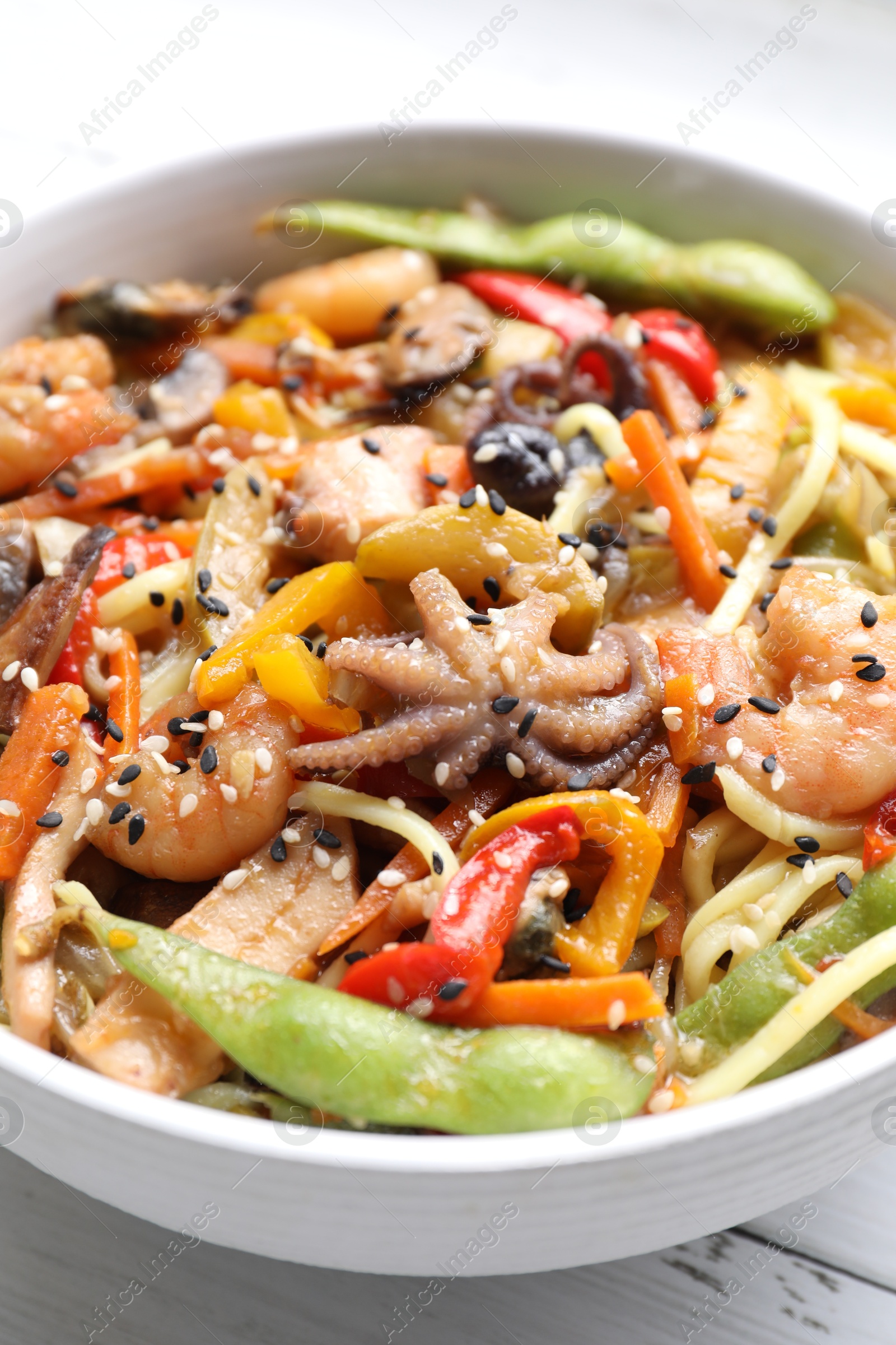 Photo of Stir-fry noodles with sea food in bowl on white table, closeup